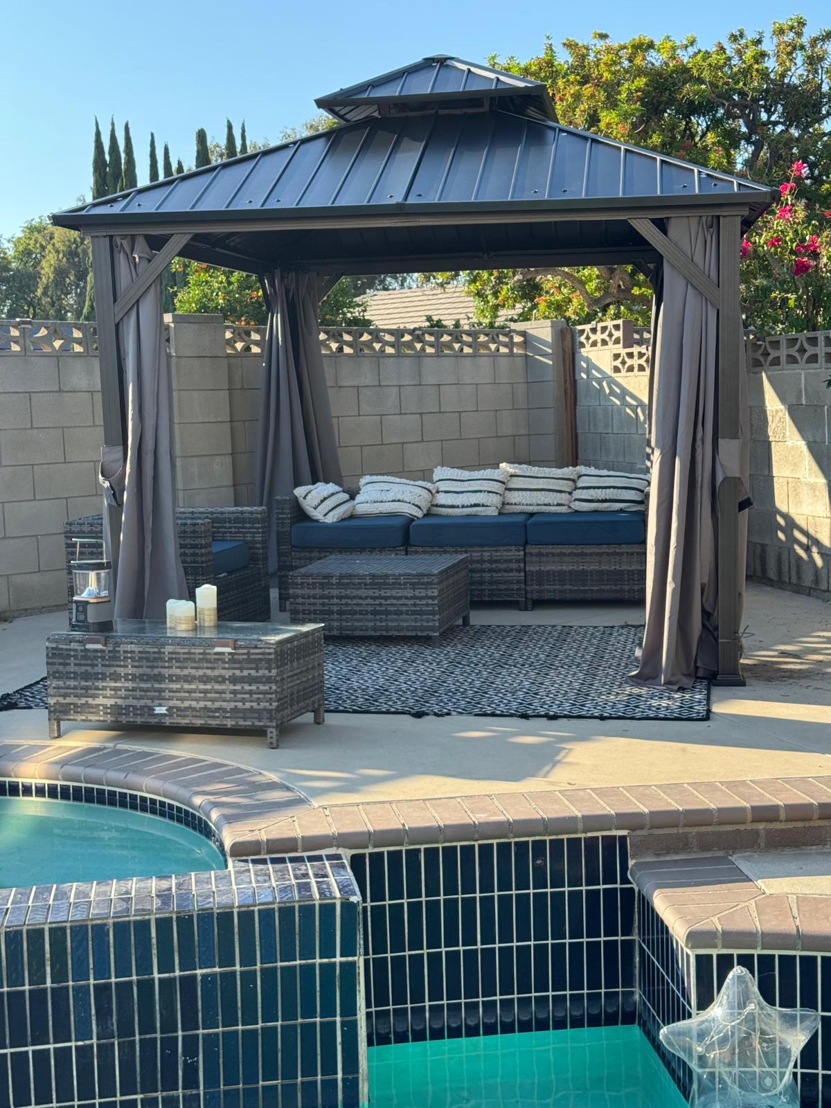 Backyard gazebo with covered seating area next to a tiled pool and spa