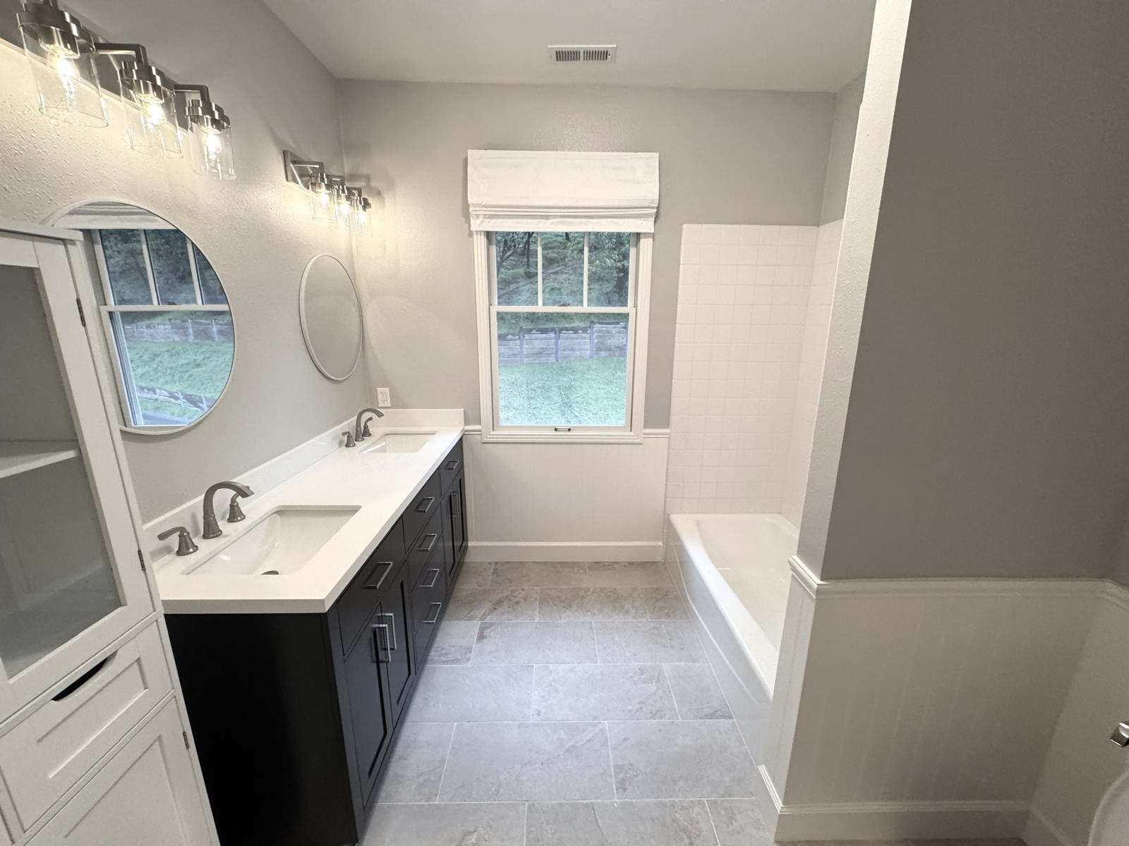 Finished bathroom with dual vanity, round mirrors, and tiled tub surround in a Thousand Oaks home